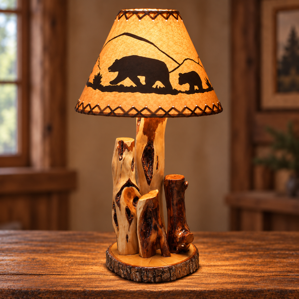Illuminated rustic bear and cub lamp shade with pine tree silhouettes and brown laced trim on lamp base