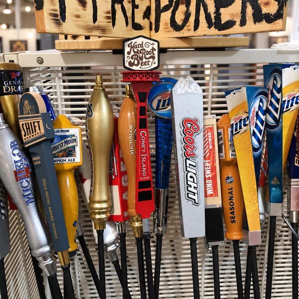 A display of multiple beer tap handles under a rustic wooden sign that reads 'FIREPOKERS' in black letters. Visible brands include Coors Light, Miller High Life, Budweiser, Miller, Schlump, and Great Lakes Brewing.