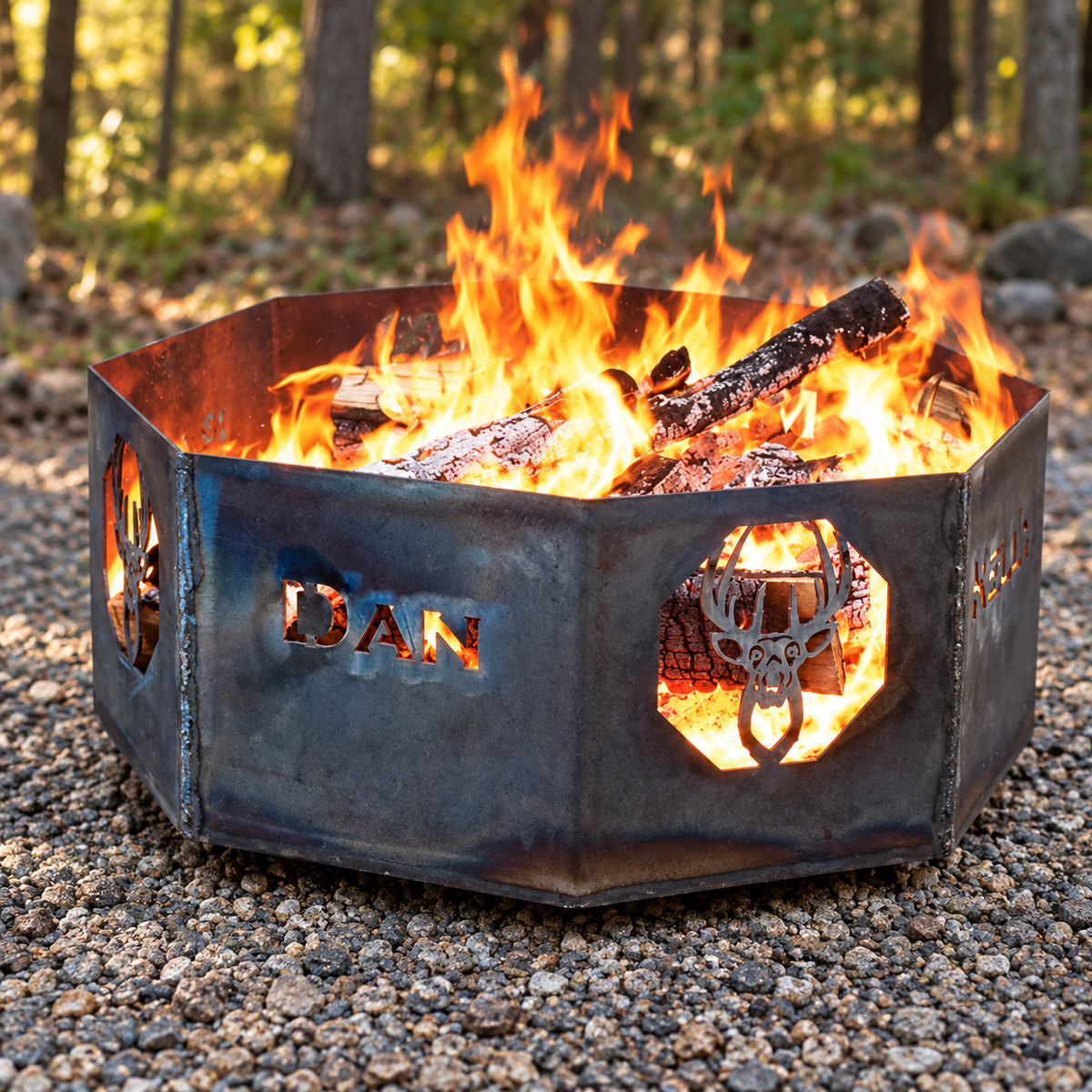 Personalized weathered-steel fire ring with a DAN name cutout and deer-skull design burning in a woodland setting.