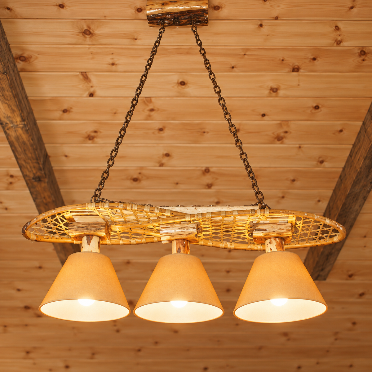 Custom handmade snowshoe chandelier with three Diamond Willow light supports and warm beige shades in a rustic pine cabin.