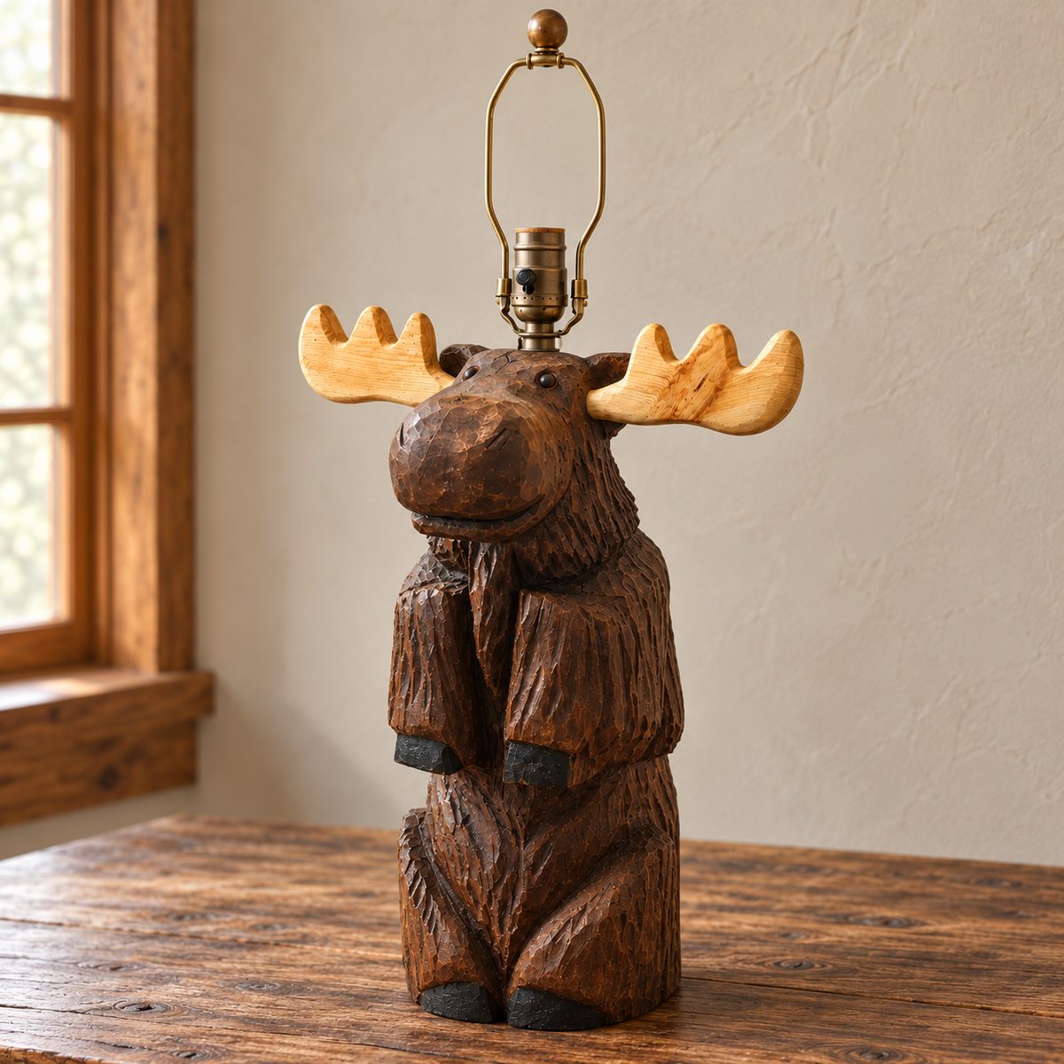 A carved wooden moose table lamp with light natural antler shades and a brass-toned metal lamp base, displayed on a rustic wooden table against a neutral wall.